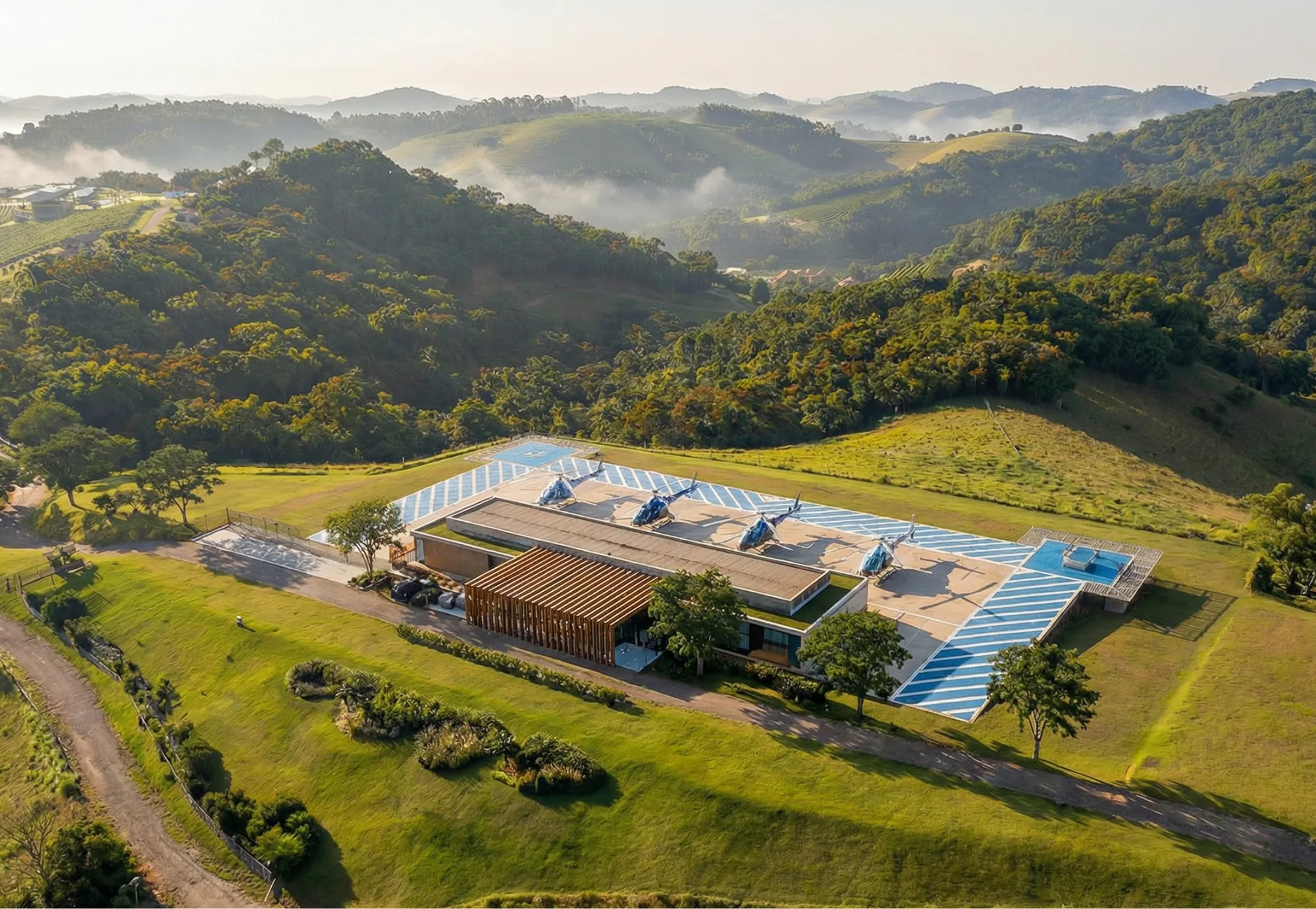 Helipuerto con helicópteros junto al pabellón de madera, conjunto implantado en el valle entre cerros verdes, vista aérea, proyecto Arsenic Arquitetos