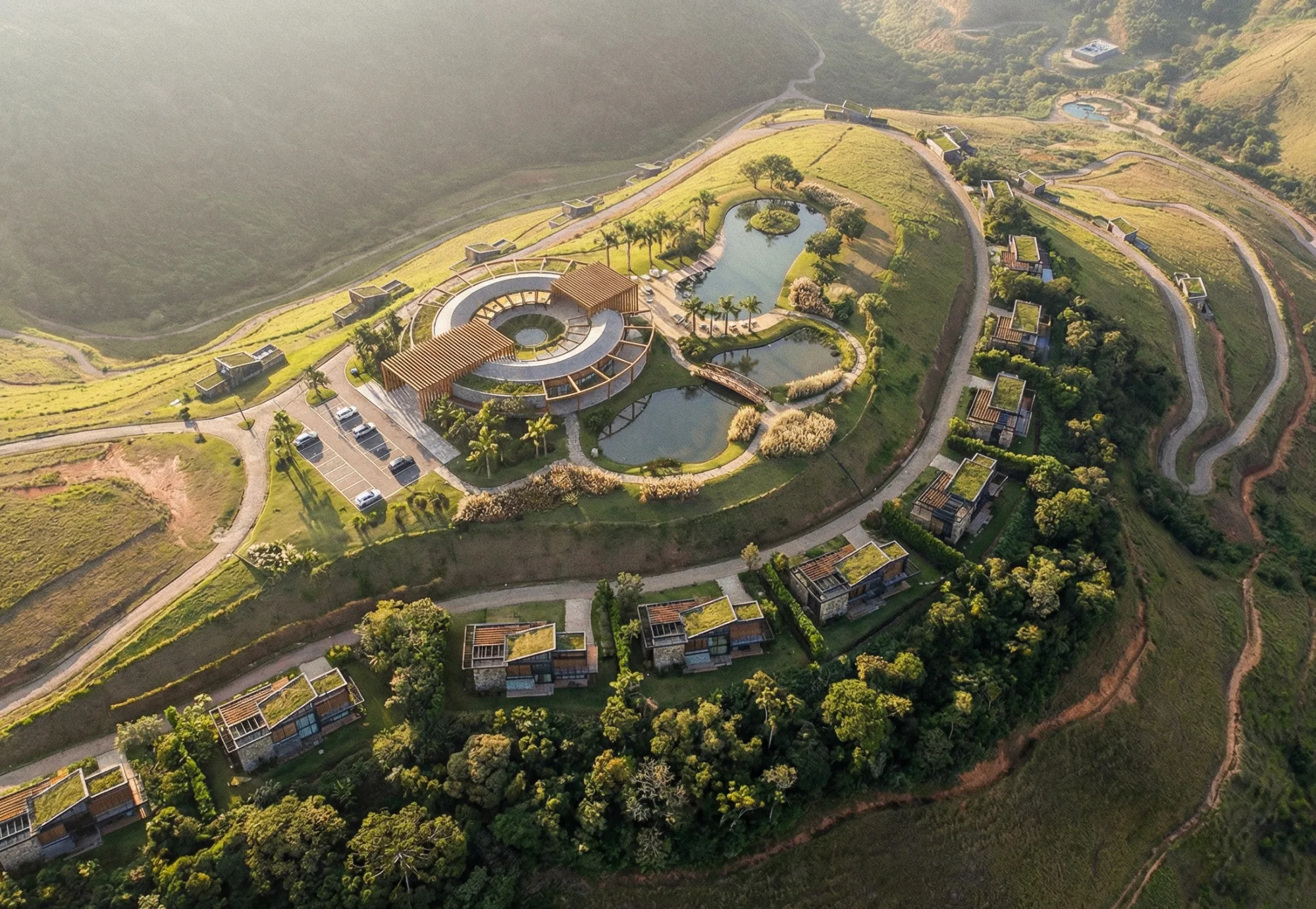 Edificio circular junto a un lago y construcciones repartidas por la ladera, vista aérea, proyecto Arsenic Arquitetos