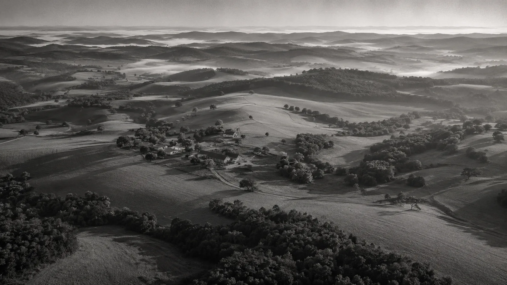 Vista aérea de uma fazenda inteira entre morros e névoa no vale ao amanhecer, o território lido como um todo em vez de loteado