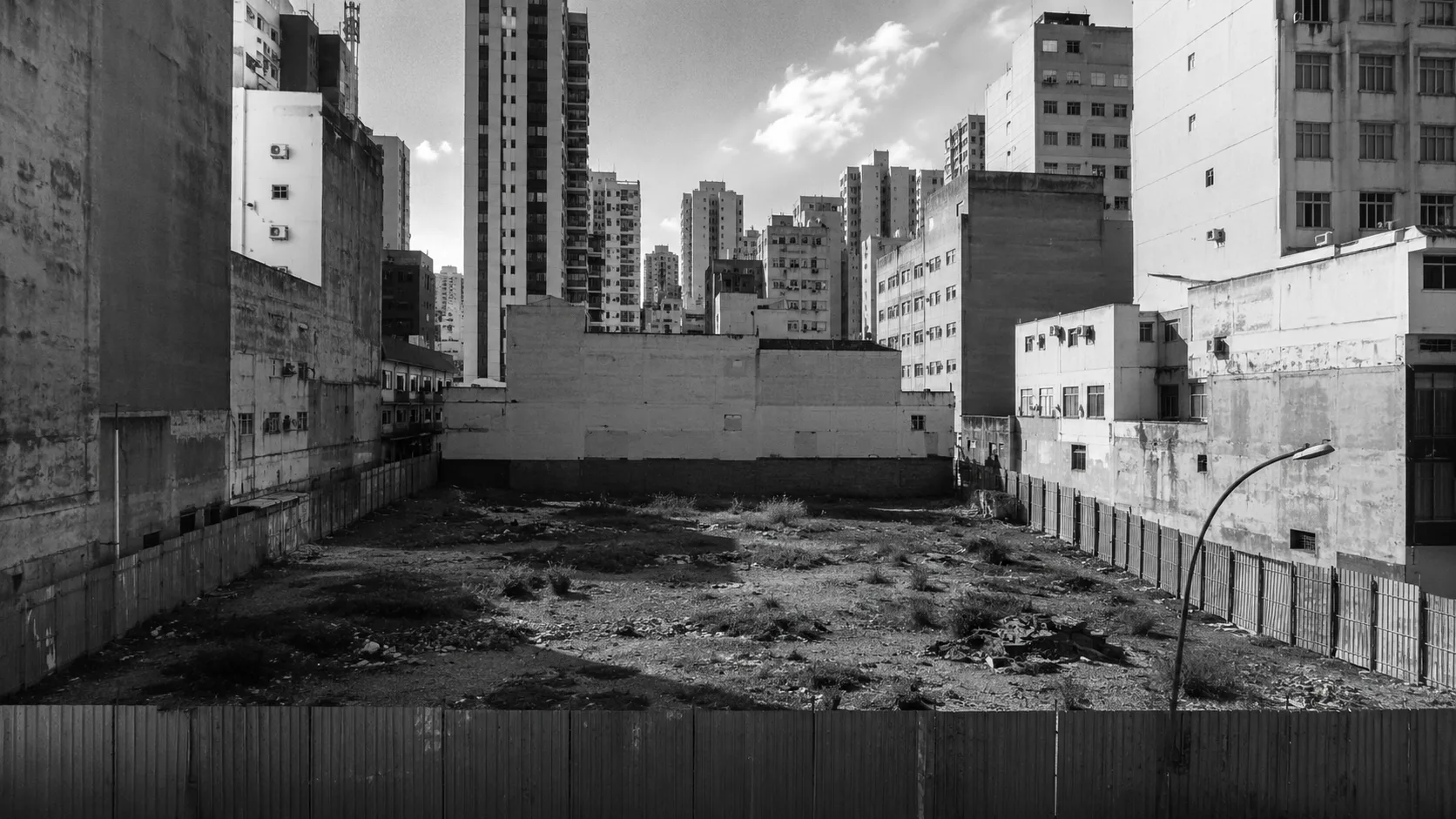 Terreno urbano vazio e murado no meio de um centro adensado de prédios altos, exemplo de imóvel ocioso que não cumpre função social