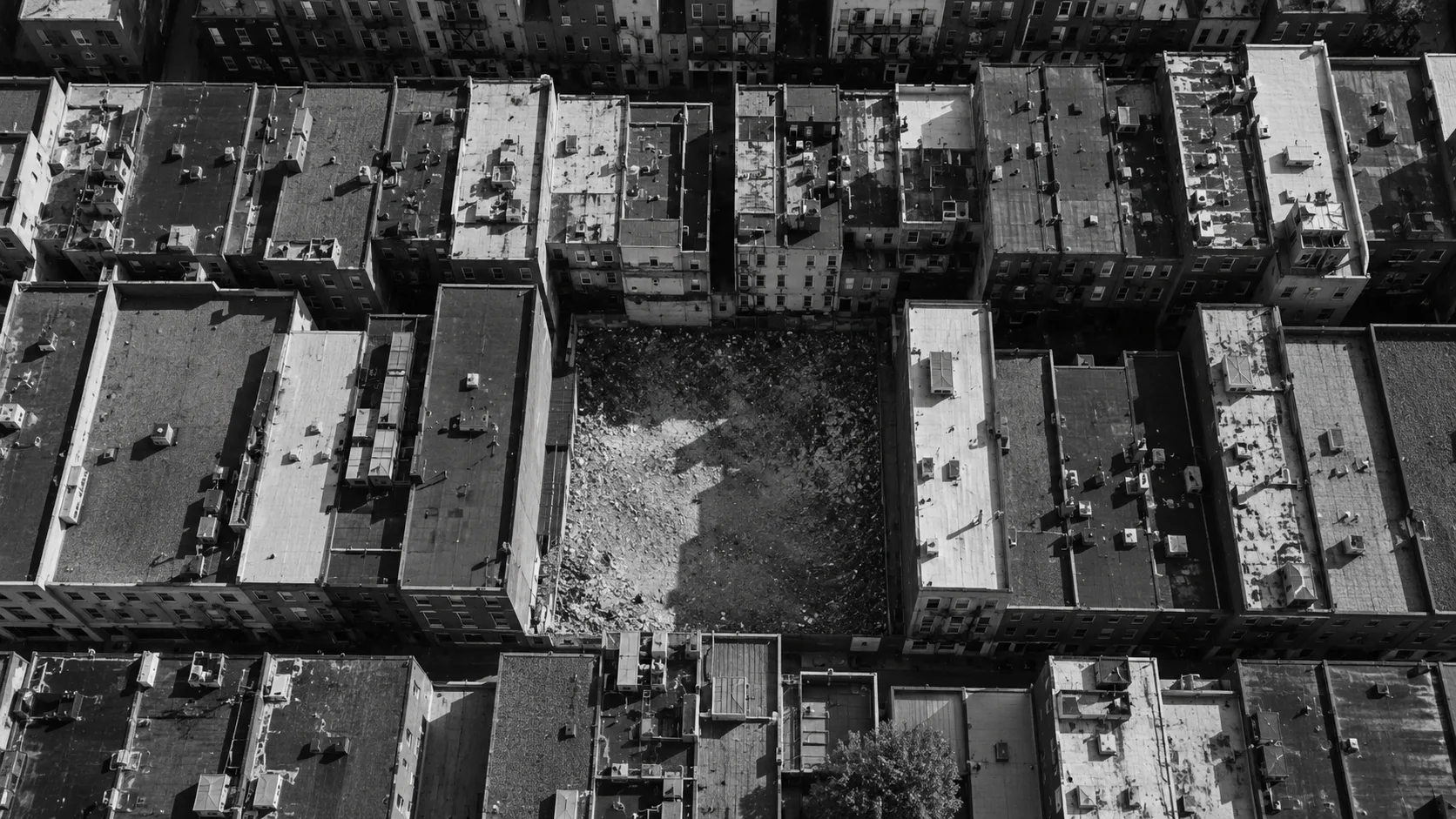 Vista aérea de uma quadra urbana densa com um terreno vazio no meio das construções, o vazio ocioso cercado de edifícios