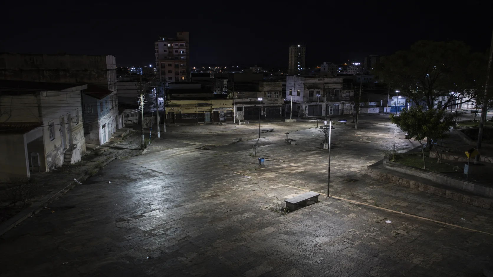 Praça grande vazia e mal iluminada à noite, vista do alto, com aspecto inseguro