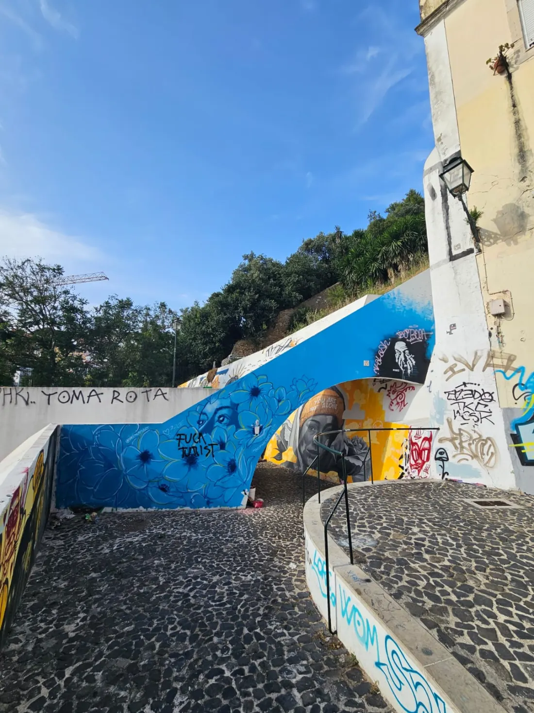 Javno stepenište između potpornih zidova potpuno oslikanih muralima i preko njih nabacanim grafitima, kraj Graça, Lisabon