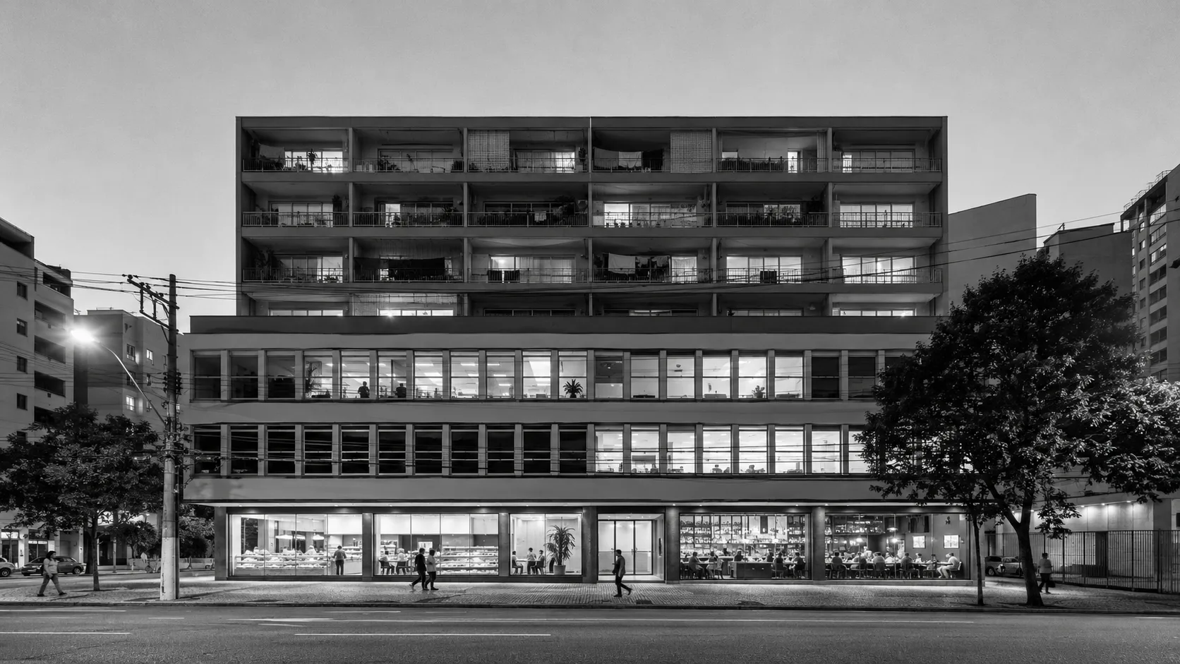 Edifício de uso misto à noite, lojas iluminadas no térreo, escritórios no meio e apartamentos com varanda no topo, cidade do Sudeste do Brasil