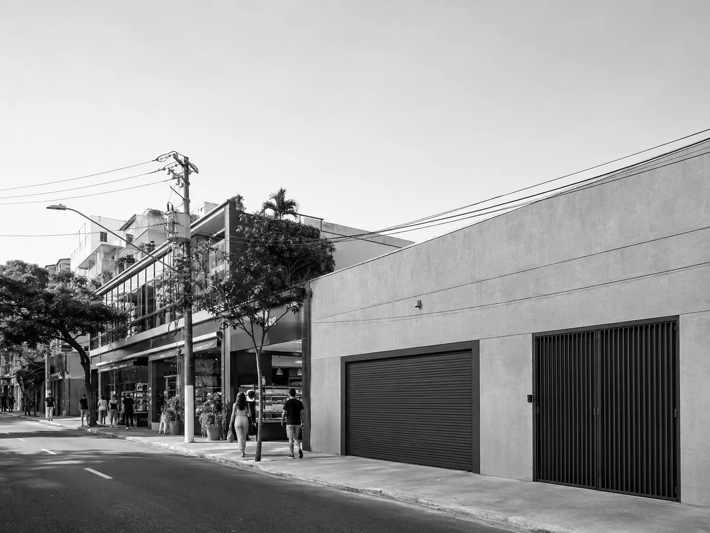 Rua de cidade do Sudeste do Brasil com comércio de térreo movimentado ao fundo e uma longa empena cega com portões de garagem ao lado, exemplo de fachada morta